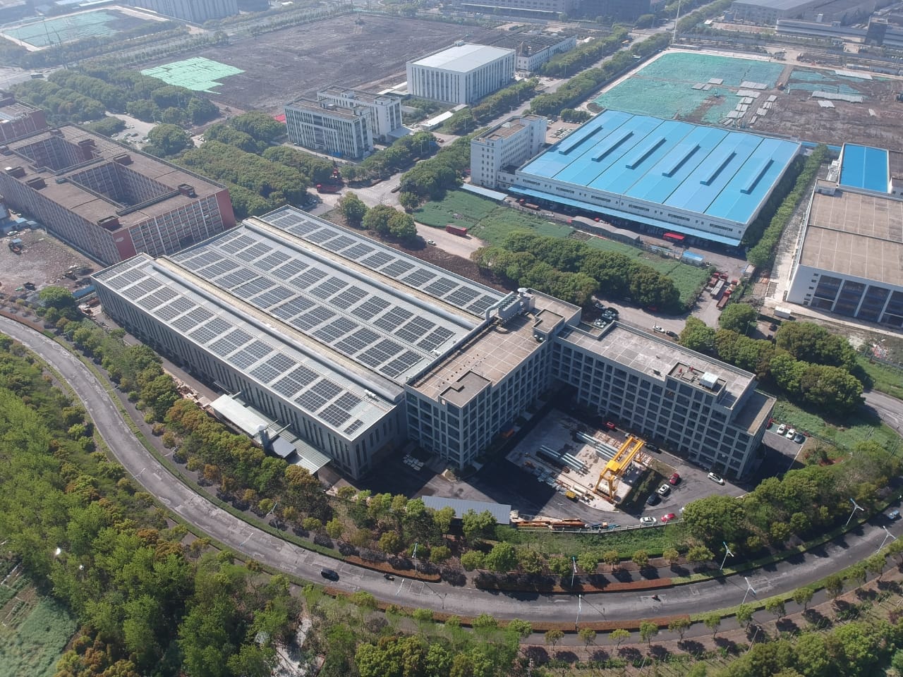 Workers and machinery processing heavy steel components inside a manufacturing base in Suzhou. The production line handles OEM steel parts, wind power component